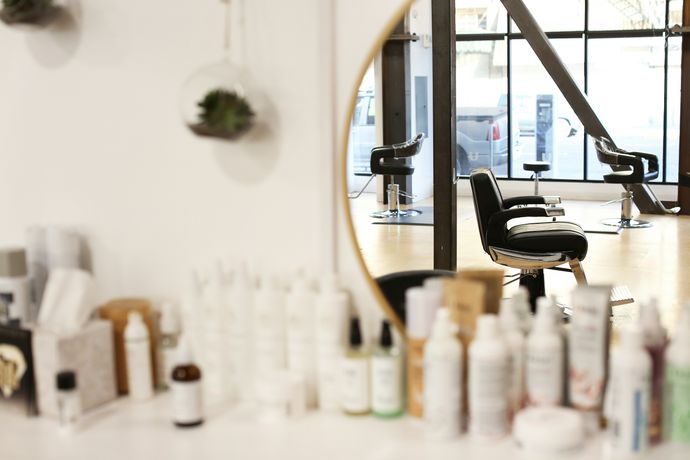 Leerer Barberstuhl, gespiegelt in einem runden Spiegel mit Messingrahmen, davor Pflegeprodukte